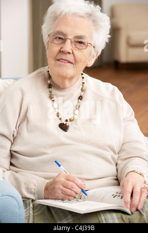 Senior donna rilassante in poltrona a casa completando il cruciverba Foto Stock