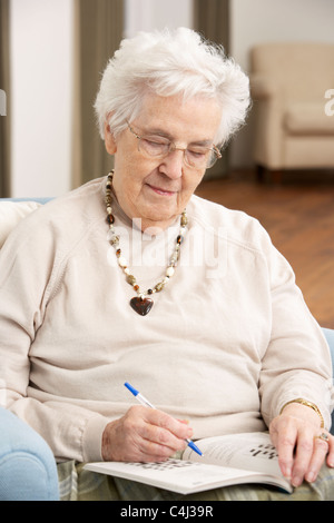 Senior donna rilassante in poltrona a casa completando il cruciverba Foto Stock