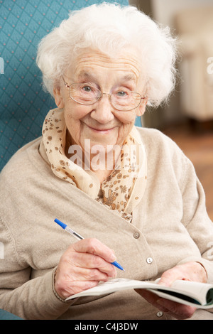 Senior donna rilassante in poltrona a casa completando il cruciverba Foto Stock
