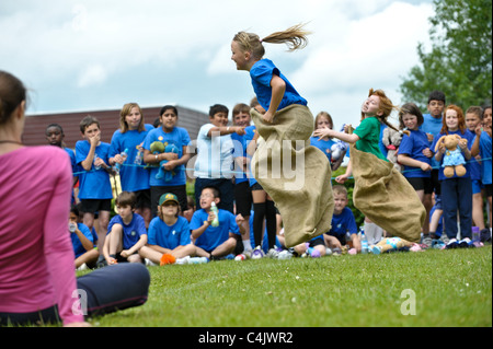 Due ragazze della scuola per competere in una scuola tradizionale giornata di sport sacco gara sul traguardo un salto in aria, capelli battenti Foto Stock