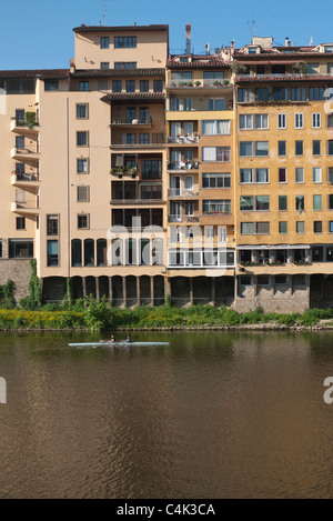 Un atleta di righe del suo passato scull edifici sul fiume Arno in inizio di mattina di luce. Foto Stock