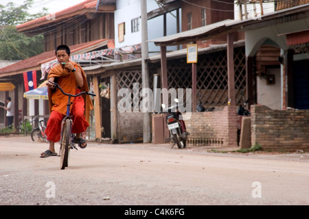 Un giovane monaco buddista è una bicicletta su una strada di sporco nelle zone rurali del Laos comunista. Foto Stock