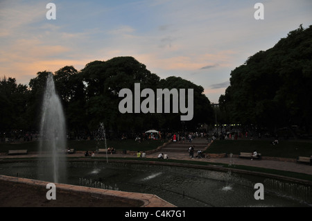 Dark crepuscolo serale vista della fontana la folla di gente seduta in piedi sotto gli alberi, Plaza Independencia, Mendoza, Argentina Foto Stock