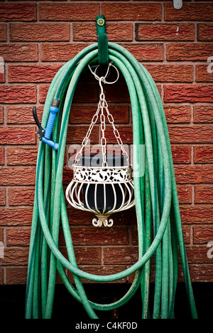 Una casa comune tubo da giardino avvolto a spirale e da appendere al muro in mattoni con appeso al di sotto della piantatrice. Foto Stock