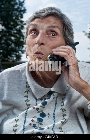 Una donna anziana, con uno sguardo di sorpresa sul suo volto, colloqui su un telefono cordless. Foto Stock