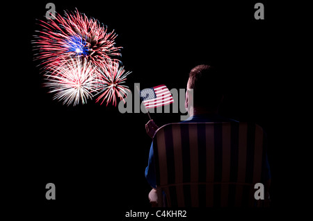 Un uomo guarda uno spettacolo di fuochi d'artificio mentre sventola una bandiera americana. Foto Stock