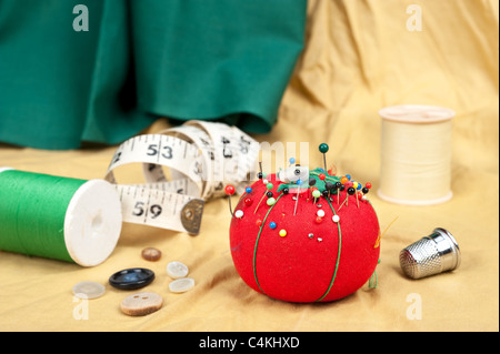 Una tabella di cucitura con pulsanti, pin cuscino, metro a nastro e ditale. Foto Stock