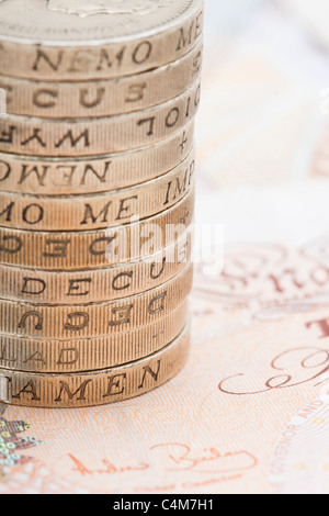 Primo piano della pila / pila di una libbra di monete al di sopra di dieci Pound note Foto Stock
