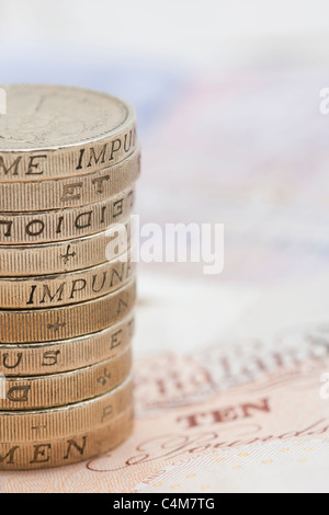 Primo piano della pila / pila di una libbra di monete al di sopra di dieci Pound note Foto Stock