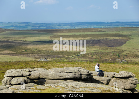 In orizzontale ampia angolazione di un uomo prendendo fotografie della vista da Haytor, fieno Tor, sul Parco Nazionale di Dartmoor su un giorno d'estate Foto Stock