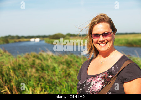 Attraente di giovani donne sorrisi a fotocamera su una luminosa giornata d'estate, mentre si sta in piedi sul bordo del Norfolk Broads Foto Stock