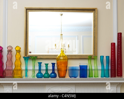 Una raccolta di diversi colori e forme di bottiglie e vasi da vetro riciclato in una fila su un da caminetto da uno specchio Foto Stock