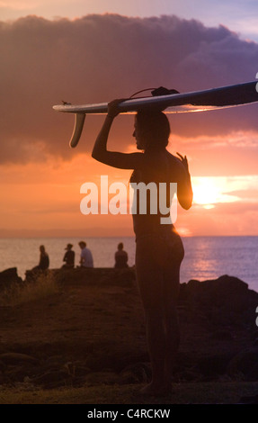 Femmina di bilanciamento del surfista con la tavola da surf sul suo capo al tramonto, Kauai, Hawaii, STATI UNITI D'AMERICA Foto Stock