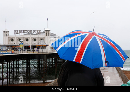 Un uomo in possesso di un Unione Jack ombrello si affaccia verso il Molo di Brighton in Inghilterra. Foto Stock