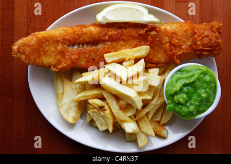 Un piatto di pesce e patatine è servita con fiacco di piselli e di un cuneo di limone. Foto Stock