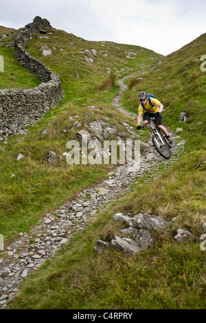 Mountain Biker scorre giù per un sentiero roccioso in Snowdonia, Wales, Regno Unito Foto Stock