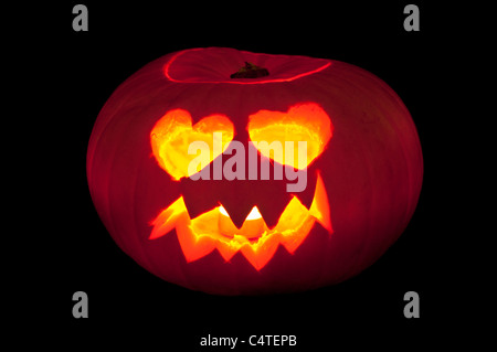 Faccia con gli occhi a forma di cuore scolpiti in una zucca per fare lanterna di Halloween su sfondo nero Foto Stock