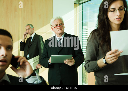 Executive che guarda lontano nel pensiero con tavoletta digitale in mano, circondato da colleghi di occupato Foto Stock