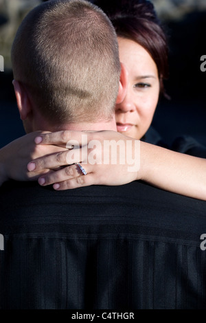 Una bella giovane donna avvolge il marito o fidanzato. Profondità di campo con il focus sul diamante anello di fidanzamento. Foto Stock
