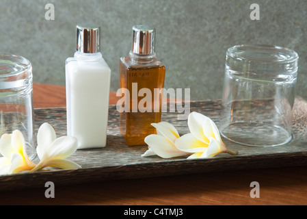 Bottiglia di profumo e i bicchieri sul vassoio con fiori di frangipani Foto Stock