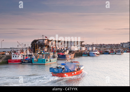 Bridlington al tramonto (barca da pesca che entra nel porto, barche ormeggiate dal molo, banchina di pesce, mare calmo) - panoramica città della costa dello Yorkshire del Nord, Inghilterra, Regno Unito. Foto Stock