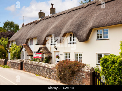 Cottage con tetto in paglia UK - Vecchio inglese semi indipendente / terrazza in un piccolo villaggio, un cottage con tetto in paglia con un cartello per la vendita, Inghilterra UK Foto Stock