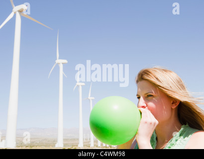 Stati Uniti, California, Palm Springs, Coachella Valley, San Gorgonio Pass, Donna insufflazione del palloncino verde con turbine eoliche in background Foto Stock