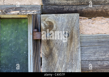 Rustico finestra arrugginita cerniera su un Weathered Log Cabin Foto Stock