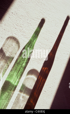 Ombre di verde e marrone di vino o di bottiglie di birra e due nottolini chiara sulla trama parete bianca Foto Stock