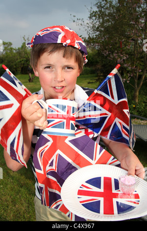 Giovane ragazzo sorridente adornata con Union Jack Flag, pur avendo una torta e tazza di tè. Foto Stock