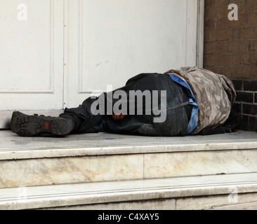 Un uomo senza tetto dorme in modo irregolare a una porta in una città del Regno Unito. Foto Stock
