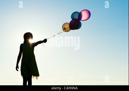 Silhouette di una ragazza giovane azienda di palloncini colorati al tramonto Foto Stock