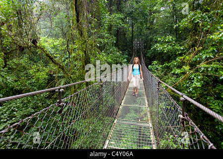 Una donna cammina attraverso un ponte di sospensione in Costa Rica. Foto Stock