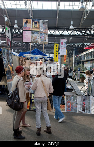 I giovani consumatori di fronte a un'arte stallo in Old Spitalfields Market in Bishopsgate, London, England, Regno Unito Foto Stock