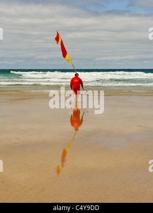 Un bagnino RNLI portante un flag di avviso su Fistral Beach in Newquay. Foto di Gordon Scammell Foto Stock