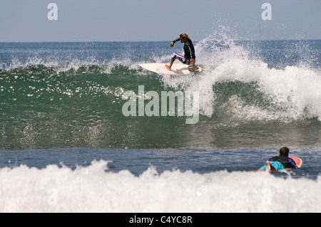 Un giovane maschio adulto surfer cavalca un bellissimo in onda, Sayulita Nayarit, Messico mentre un altro surfer pagaie in primo piano. Foto Stock