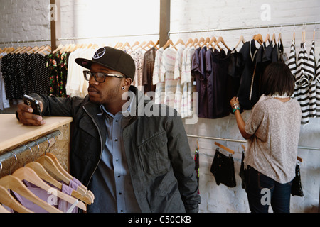 African American uomo di messaggistica di testo sul telefono cellulare in negozio di abbigliamento Foto Stock