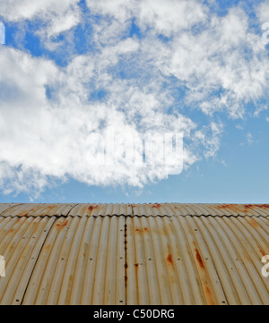 Vecchie e arrugginite weathered acciaio capanna quonset tetto contro un cielo blu con nuvole di ovatta Foto Stock