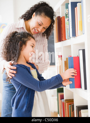 Madre aiutare mia figlia scegli libro sul ripiano Foto Stock