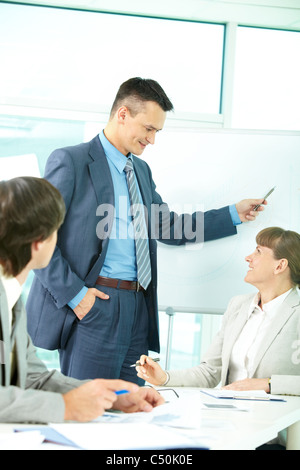Un uomo di affari che mostra qualcosa su una lavagna e guardando a un collega Foto Stock