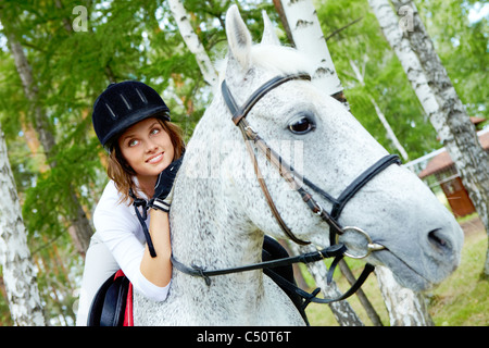 Immagine di felice jockey femmina sul cavallo di razza in esterno Foto Stock