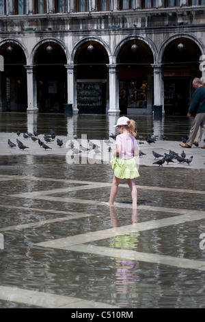 Giovani donne a piedi attraverso il crescente volume di acqua di inondazione Piazza San Marco piccioni raccolta sulla zona asciutta di allagamento del plaza in background Venezia Italia UE Foto Stock