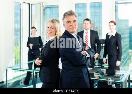 Business - team in un ufficio; il senior executive è in piedi di fronte con il suo segretario Foto Stock
