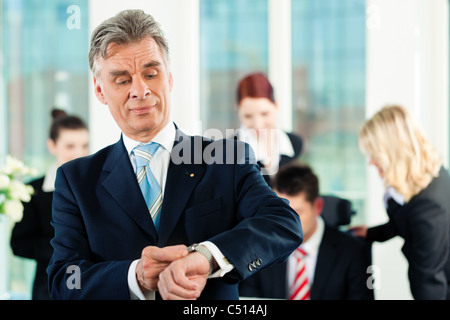 Business - team in un ufficio; il senior executive è controllare il suo orologio Foto Stock