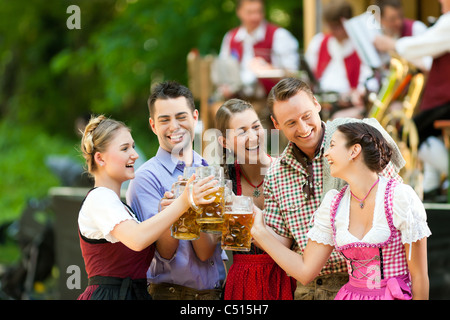 Nel giardino della birra in Baviera, Germania - Amici in Tracht, Dirndl e lederhosen e Dirndl in piedi nella parte anteriore del nastro Foto Stock