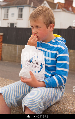 A sette anni di vecchio ragazzo mangia fish & chips sulla parete del mare in Aldeburgh , Suffolk , Inghilterra , Inghilterra , Regno Unito Foto Stock