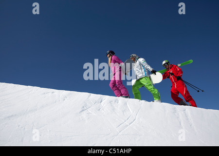 Un gruppo di tre persone con gli sci e gli snowboard camminare su per la montagna Foto Stock