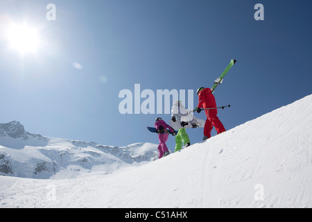 Un gruppo di tre persone con gli sci e gli snowboard camminare su per la montagna Foto Stock