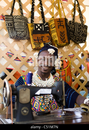 Un sorridente sarto keniota in abiti tradizionali seduti dietro una macchina da cucire Foto Stock