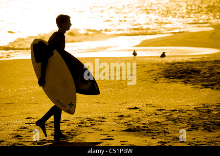 Un giovane uomo a camminare sulla spiaggia portante due schede scremato Foto Stock